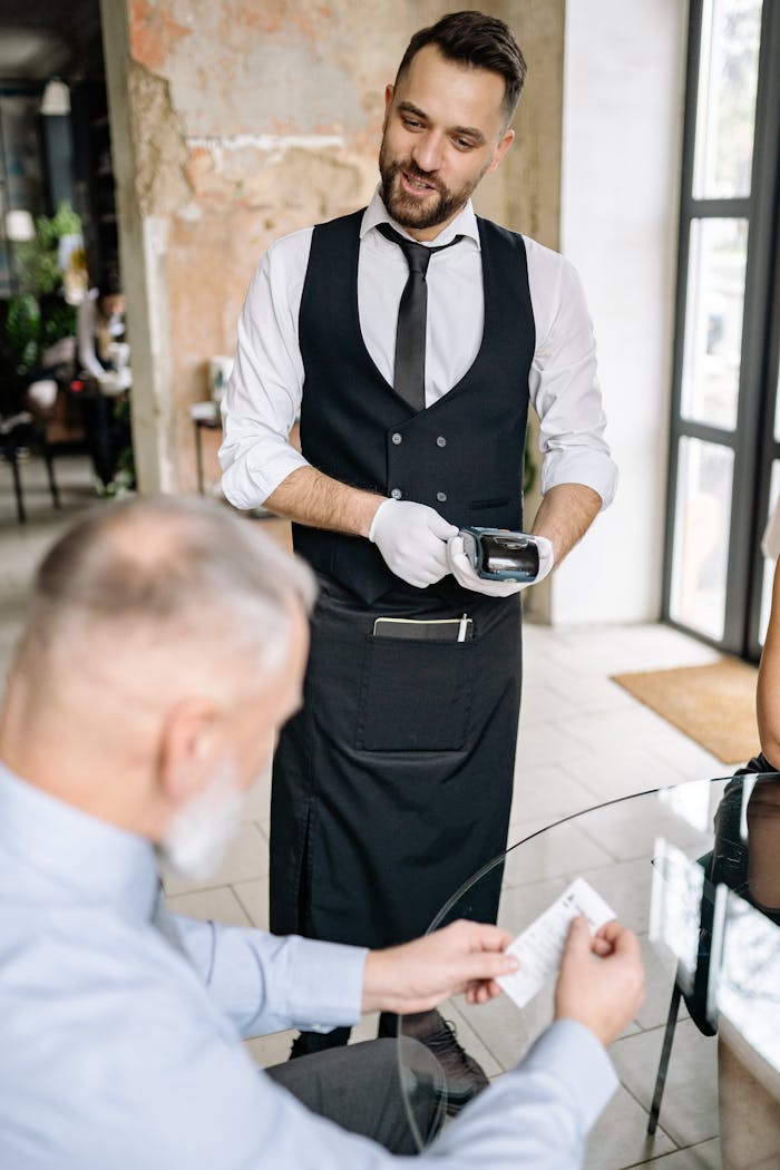 A waiter processes payment using a terminal while a customer reviews the bill, showcasing excellent service.